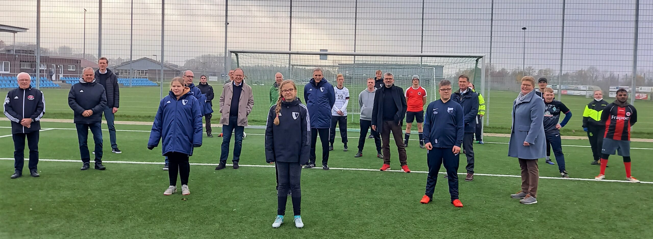 Man sieht Erwachsene und Kinder vor einem Fußballtor und auf einen Fußballfeld
