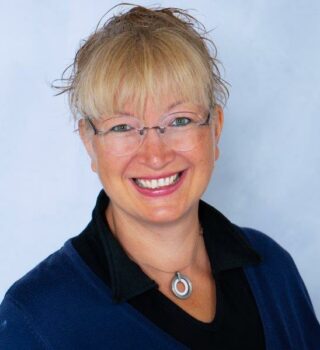 Bianca Rieken: Eine lächelnde Frau mit blonden langen Haaren mit Zopf und einer Brille. Sie trägt auch eine Kette.