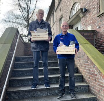 Zwei Gäste stehen draußen auf einer Treppe vor der Kamera. Sie haben jeweils ein Präsentkorb vom GPS Laden Nordseefreundlich.