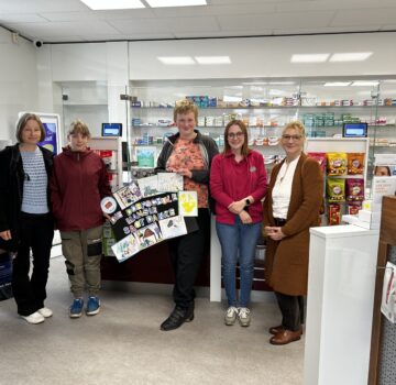 Ein buntes Plakat als Dankeschön als Übergabe an einem Laden. Man sieht auf dem Bild ein Raum, wo drei Frauen, ein Mädchen und ein Junge stehen.