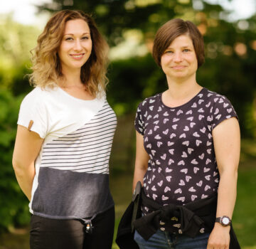 Zwei junge GPS Mitarbeiterinnen stehen draußen und lächeln in die Kamera.