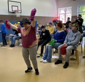 In einem Raum sitzen Menschen auf Stühlen oder stehen und schauen eine Frau beim Tanzen zu. Sie sind in einem Raum.