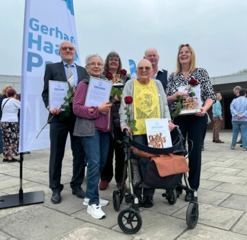GPS Gerhard Haack Preis Nominierte sind draußen auf einem Hof und halten Ihre Urkunde in den Händen. Sie lächeln. Man sieht auch neben der Gruppe eine GPS Gerhard Haack Preis Flagge.