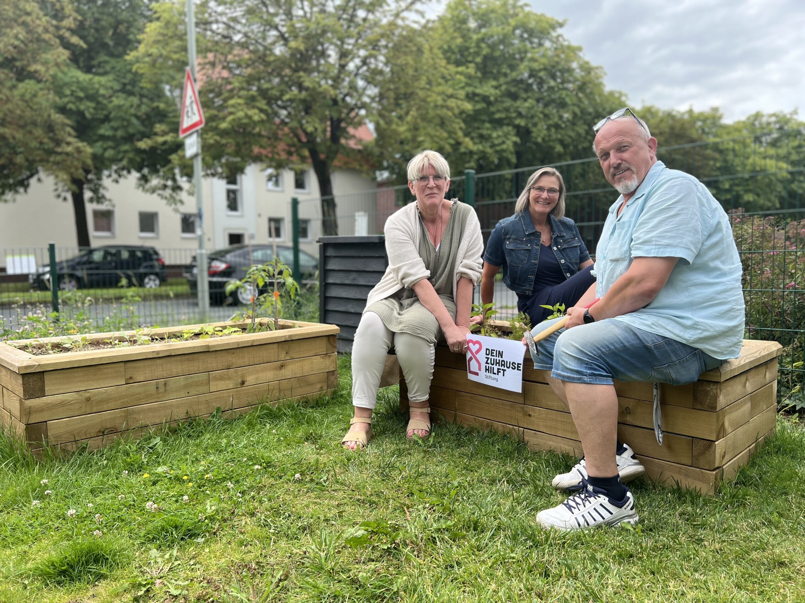 Drei GPS Mitarbeiter und Mitarbeiterinnen vom Familienzentrum Nord draußen im Garten bei sonnigen Wetter. Sie werben für eine Stiftung "Förderung Stiftung Dein Zuhause hilft.