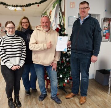 Gruppenfoto mit zwei GPS Mitarbeiter, eine junge Frau und einen Mann im Familienzentrum Nord. Ein GPS-Mitarbeiter vom Familienzentrum Nord erhält eine Spendenurkunde und zeigt mit der Hand seinen Daumen hoch.