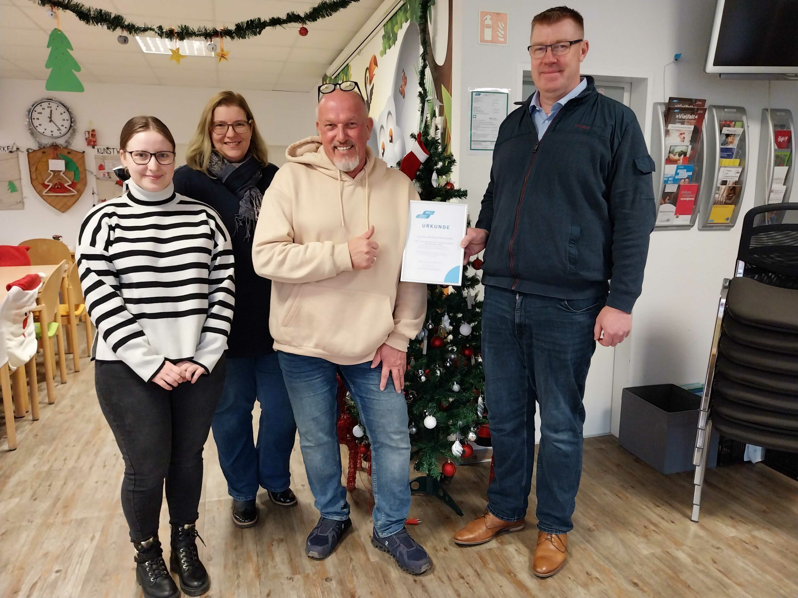 Gruppenfoto mit zwei GPS Mitarbeiter, eine junge Frau und einen Mann im Familienzentrum Nord. Ein GPS-Mitarbeiter vom Familienzentrum Nord erhält eine Spendenurkunde und zeigt mit der Hand seinen Daumen hoch.