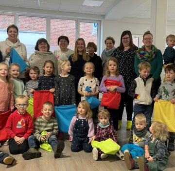 Gruppenfoto mit Erzieherinnen und Kinder eines Kindergartens. Ein paar kleine Kinder halten bunte Stoffbeutel in ihren Händen.