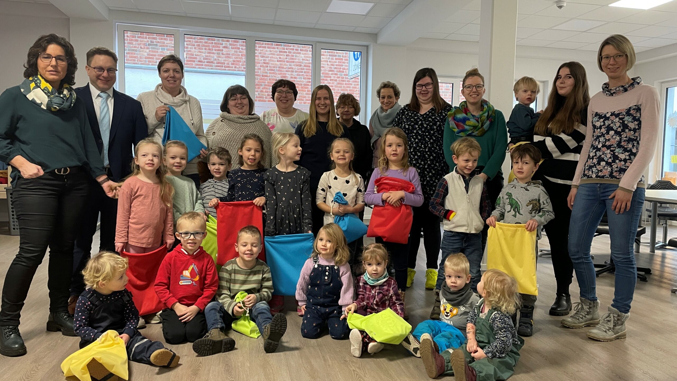 Gruppenfoto mit Erzieherinnen und Kinder eines Kindergartens. Ein paar kleine Kinder halten bunte Stoffbeutel in ihren Händen.